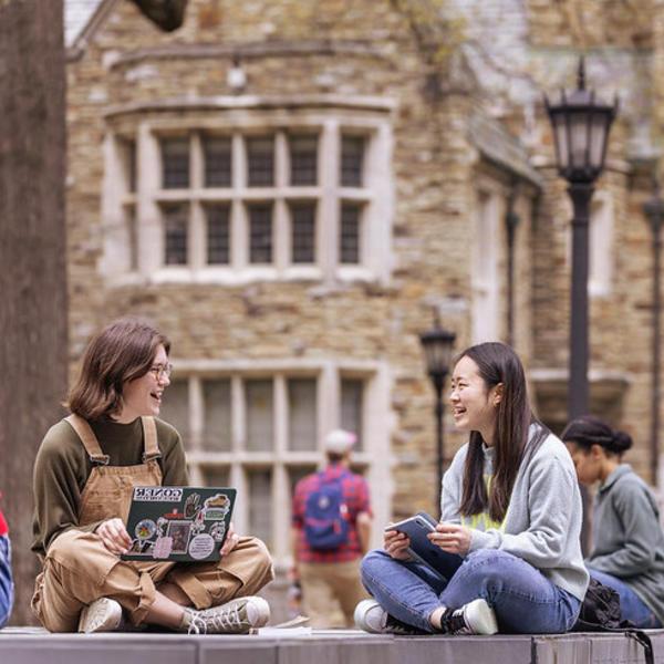 Students gather, talking, in front of a large collegiate gothic building.