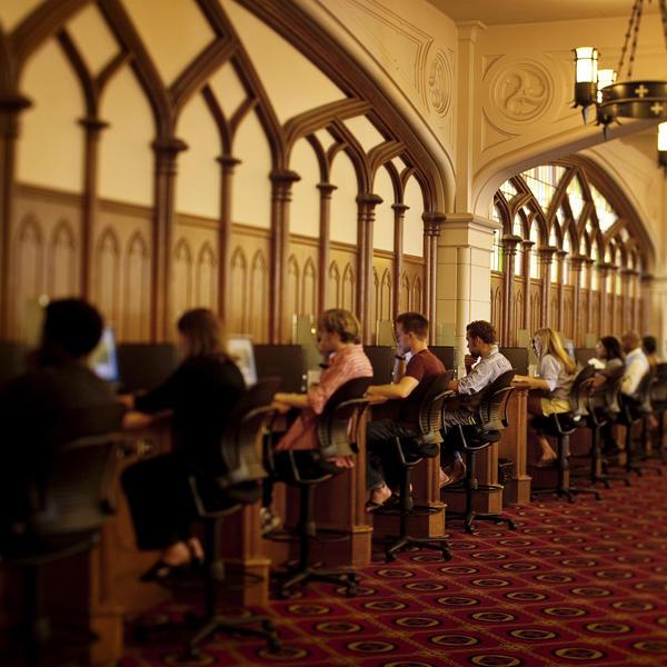 students sit at a bank of computers in a Gothic library